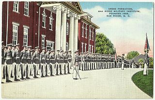 Estudiantes con uniforme de gala gris y blanco parados frente a un edificio de ladrillo rojo oscuro con altas columnas blancas.