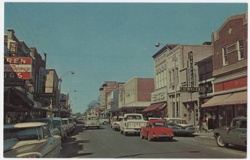Postcard image of Evans Street in Greenville, N.C. There are several older model cares on the street. Some cars parked on the street in front of large buildings.
