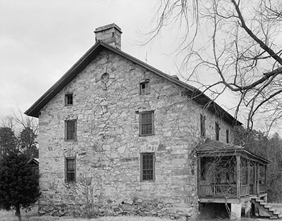 A black and white photo of the a stone and brick home. The back or front of home has stairs attached a porch