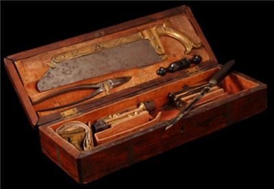 An amputation Kit with pliers, a saw, and other tools. Items all have a brown finish placed in a small box. 
