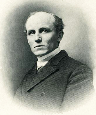 John Carlisle Kilgo from the chest up. He is wearing a dark tuxedo coat, dress shirt, and white bow tie.  His hair is short and thinning on top.  His body is angled to left, he is facing forward with a serious expression.