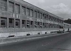 A large warehouse with the name "White Furniture Company" written across the front. It as several large windows and an empty parking lot 
