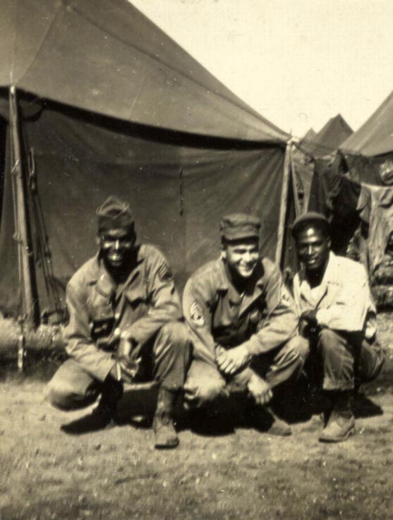 This is a black and white print of soldiers crouching with tents in the background, Fort Francis E. Warren, Wyoming, 1943. Soldiers from left to right are "unidentified," First Sergeant Southall, and Odra W. Bradley.