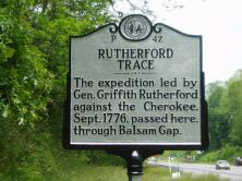 Image is the historic mile marker for Rutherford Trace. Text reads as follows: "Rutherford Trace. The expedition led by General Griffith Rutherford against the Cherokee. September 1776, passed her through Balsam Gap.