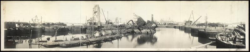 Photo depicting the destroyed battleship, U.S.S. Maine. Pieces of it are in a harbor being salvaged.