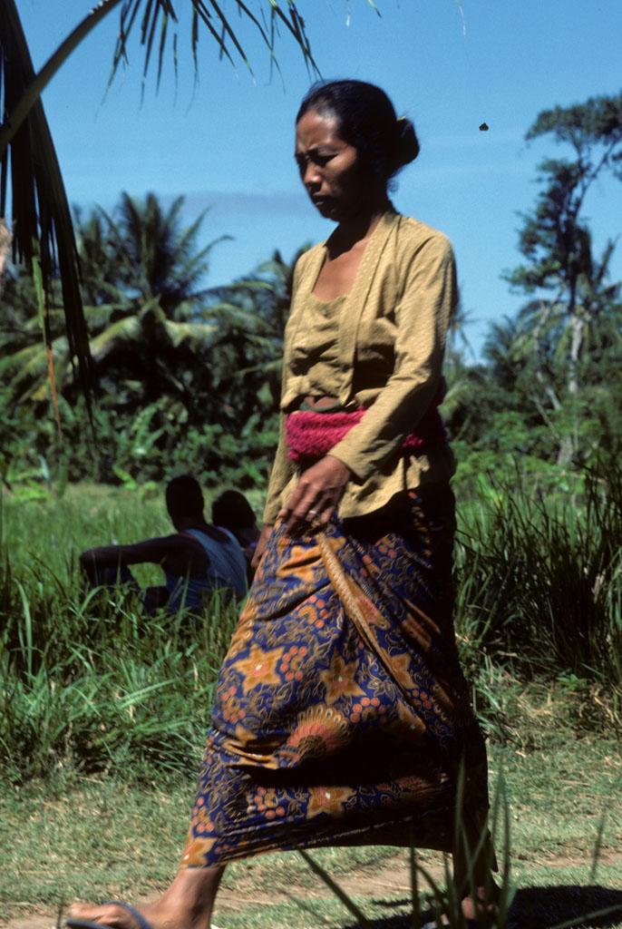 Balinese woman in sarong walks past rice field | NCpedia