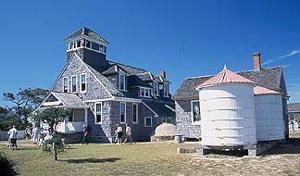 A wooden building sits in a sandy grass plot.