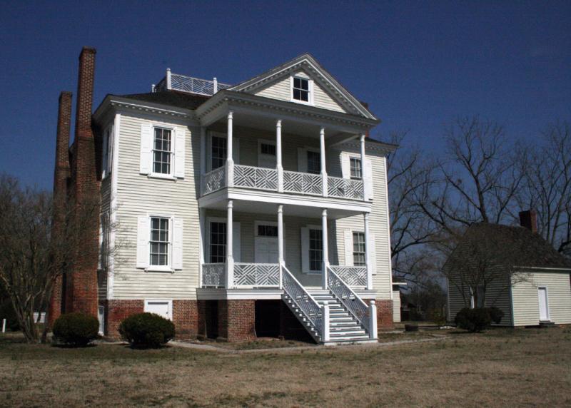 A two-story white house. It is against a clear sky. It has two chimneys and a balcony on top. 
