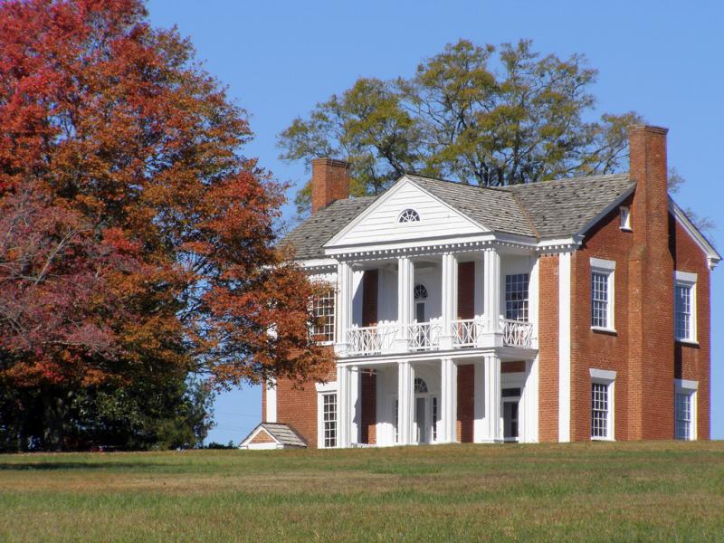 Vann House. It is sunny and there are trees. The house is two story, brick. With white columns in front. 