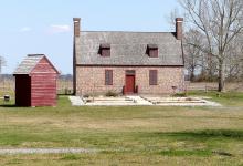 Newbold White House. Brick house with wood shed. It is a sunny day and the house sits on a mowed lawn. 