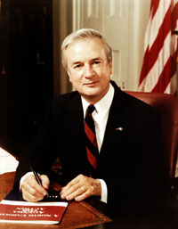 Photo of James Baxter Hunt, Jr. seated at desk with American flag in background.