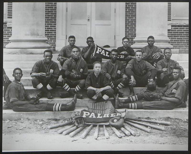 The photograph shows twelve students from the Palmer Institute baseball team. Included in the picture is their equiment, bats, gloves, basesball, protective gear, and a banner.