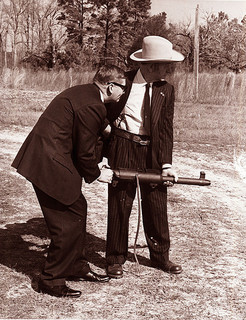Governor Terry Sanford and David Marshall "Carbine" Williams with a machine gun. They are both wearing suits.