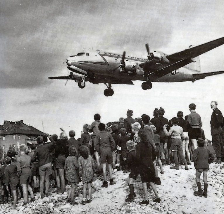 A cargo plane delivers supplies to a hillside full of people. Photo.
