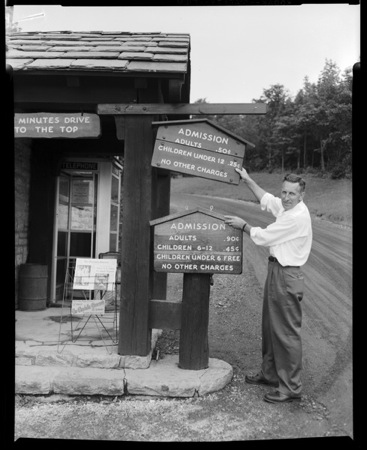 A man exchanges one sign for another at a visitor's booth. Black and white photo.