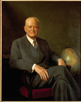 Herbert Hoover. He is sitting in a chair next to a globe. Wearing a suit with short hair.