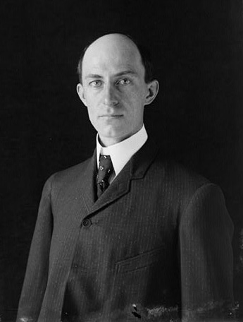 Wilbur Wright. He has no hair and looks serious. He is wearing a suit.