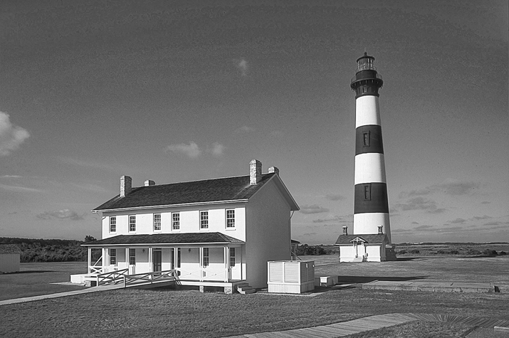 Bodie Island Lighthouse and keeper's quarters. A striped black and white lighthouse stands beside a wooden house.