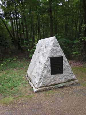 A stone triangle sits at a woodline.