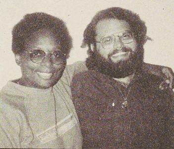 Mandy Carter hugging Marlon Garren. They are both wearing hoodies and glasses, while also smiling.