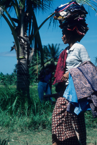 Balinese cloth vendor carries folded wares on her head