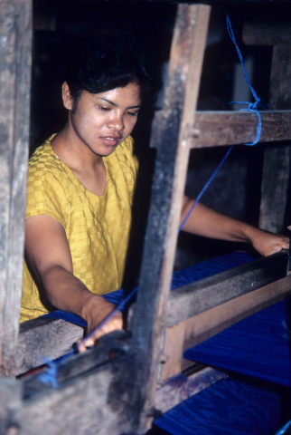 Balinese woman weaves blue cloth on a mechanical loom