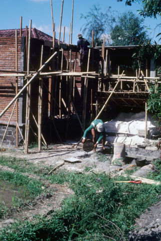 Balinese men climb bamboo scaffolds to build brick house