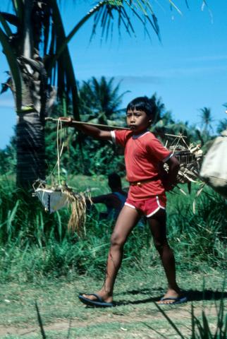 Balinese boy in red clothes carries loads in baskets hung on a shoulder board