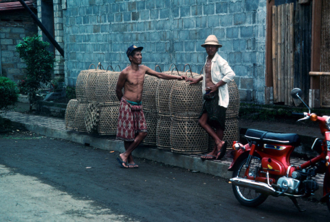 Two men standing along road with rows of cock baskets