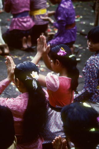 Women and girls kneel with hands held high in prayer at temple festival