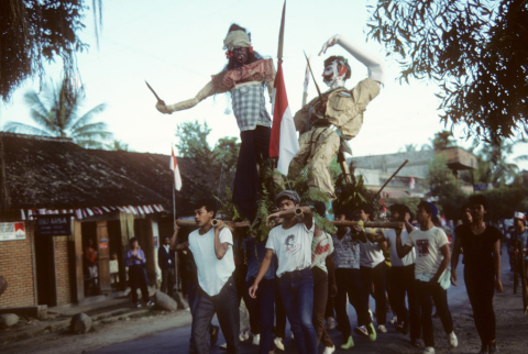 Young men carry parade float showing an Indonesian revolutionary fighting Dutch man