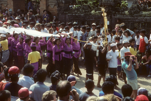 Women in funeral procession hold long white cloth above their heads