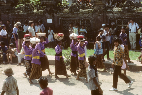 Six women in purple jackets carry offerings to cremation grounds