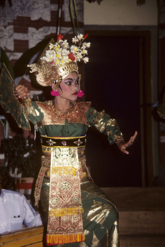 Balinese girl performing welcome dance in green and gold costume holds fan