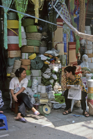 Two women sit talking outside a rope and mat shop in Hanoi