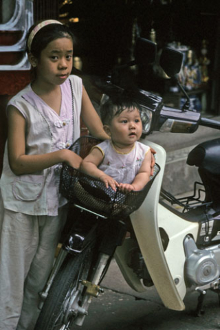 Hanoi girl tends a toddler sitting in the front basket of a motorcycle