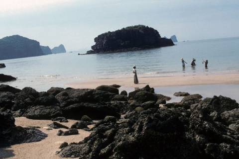 Rocky island and beach at Cat Ba with local people standing in and by the water