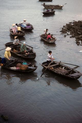 Women and children rowing small boats in the harbor at Cat Ba