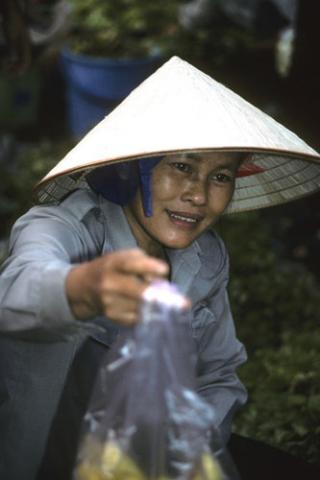 A woman in sunhat holds out bag of produce at market in Cat Ba