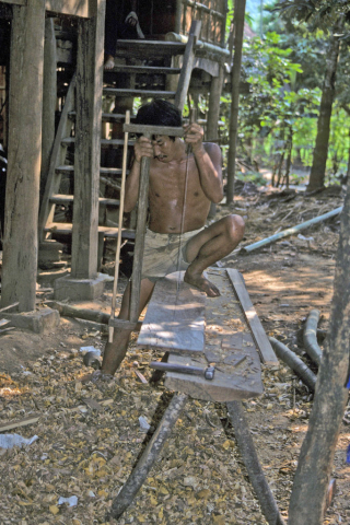 Highland man sawing board with hand tools outside house in Mai Chau