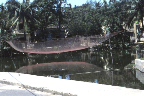 Large empty fish net suspended over harbor at Hoi An