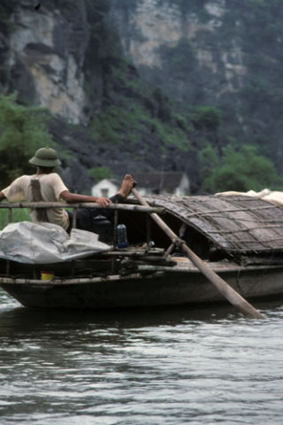 Man rowing thatched roof boat with his bare foot near Hoa Lu