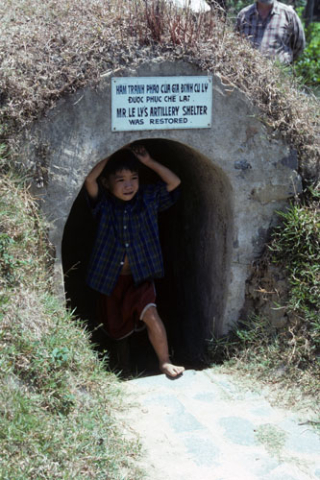 Small boy stands in entrance to underground artillery shelter at My Lai