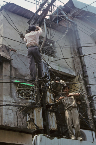 Two electricians climb on cement building to fix network of power cables in Hanoi