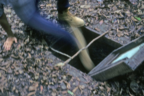 Person with leg in hinged door to Vietnam War tunnel entrance at Cu Chi