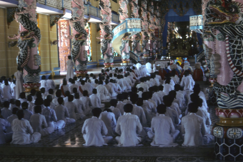 Followers dressed in white sit worshipping in Cao Dai temple at Tay Ninh