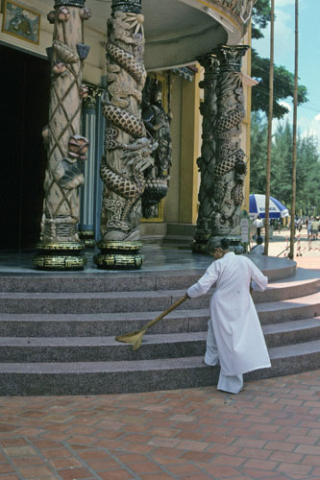 Woman in white robes sweeps veranda steps of Cao Dai temple at Tay Ninh