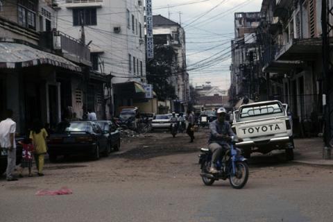 Phnom Penh side street with hotel, vehicles, electric lines, and walking family