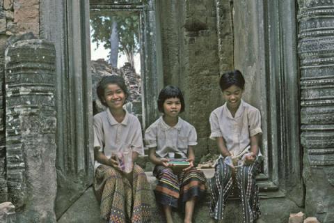 Three girls sit in stone doorway near carved columns of building at Angkor