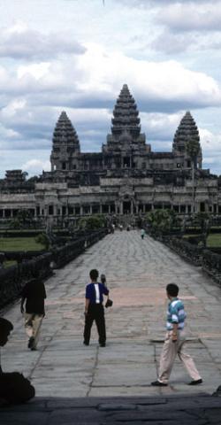 Three men walk on causeway over moat leading to Angkor Wat